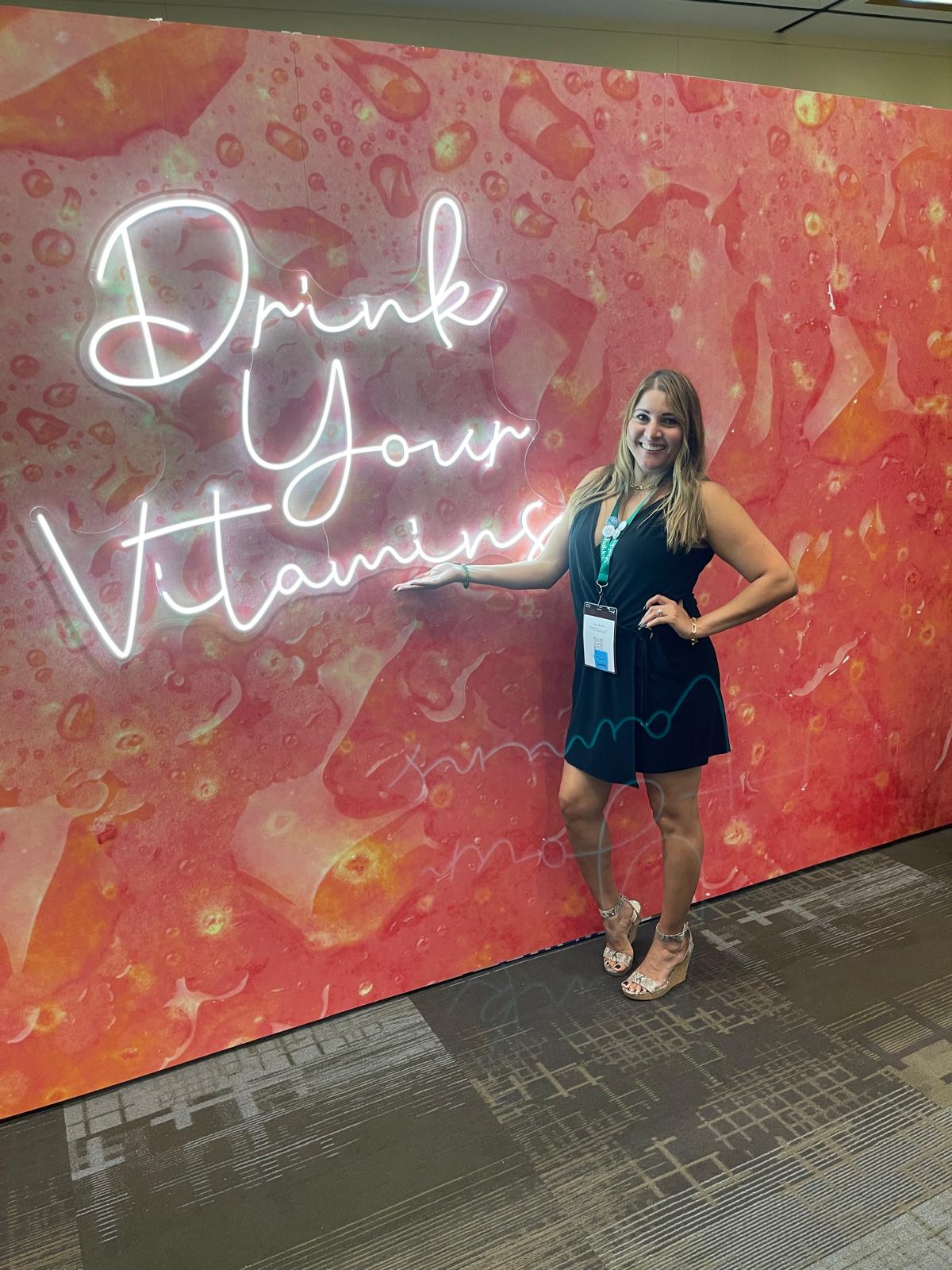 Regina posing by sign, drink your vitamins